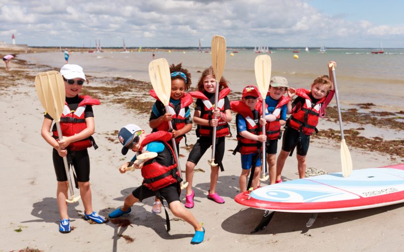 groupe d'enfants sur la plage de Langoz, équipés de gilets de sauvetage et de pagaies