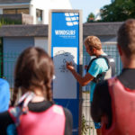 moniteur de voile dessinant unschéma sur un tableau blanc afin d'aider ses stagiaires à comprendre les diférentes allures d'une planche à voile